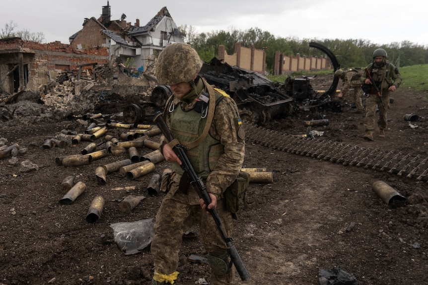 Soldiers walk near badly damaged buildings in a village. 