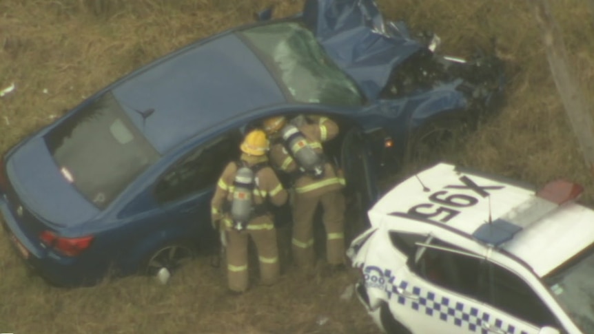 Two firefighters look into a car that has crashed on the side of a highway.