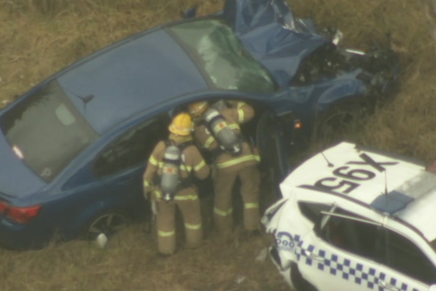 Two firefighters look into a car that has crashed on the side of a highway.