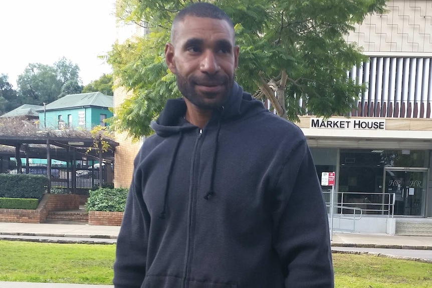 A Papua New Guinean man wearing a dark hoodie standing outside.