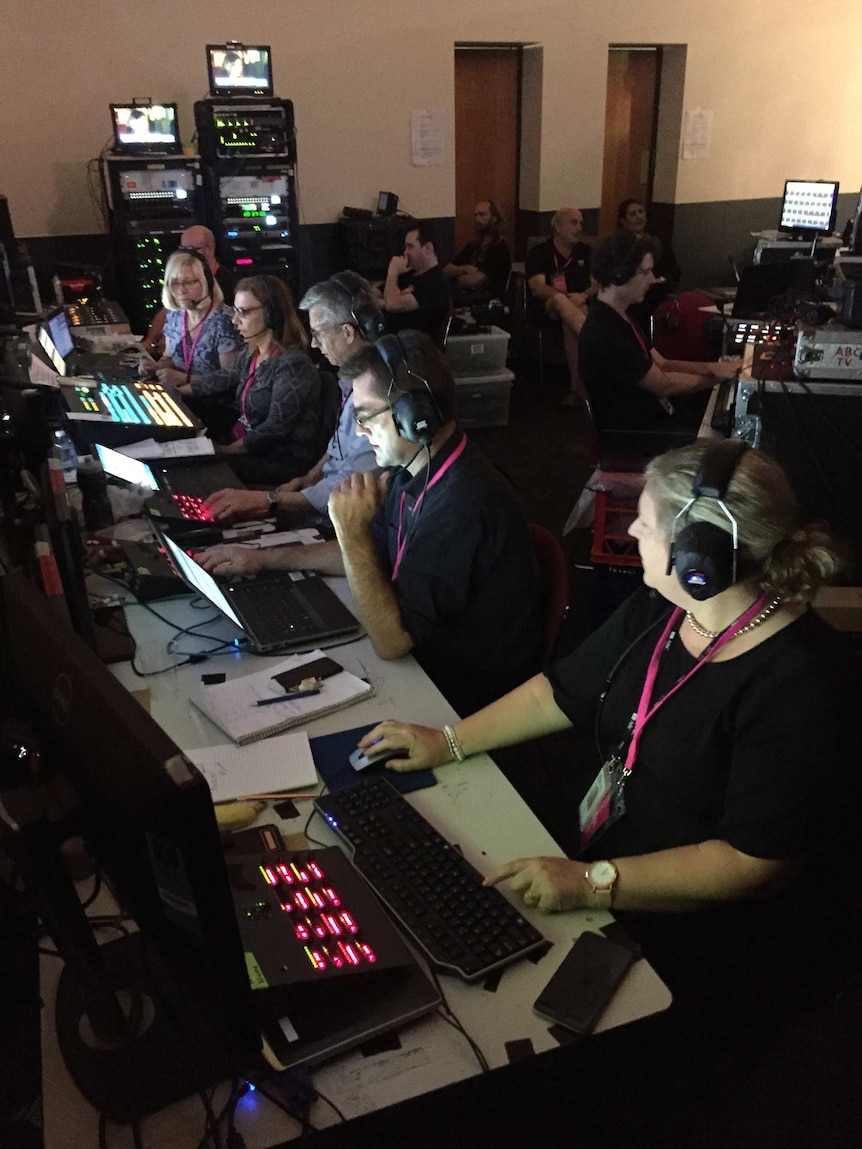 Producers and technical crew on computers and TV equipment in cramped, dark space behind set.