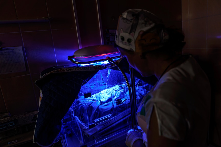 A baby is in a dark room undera  blue light. 