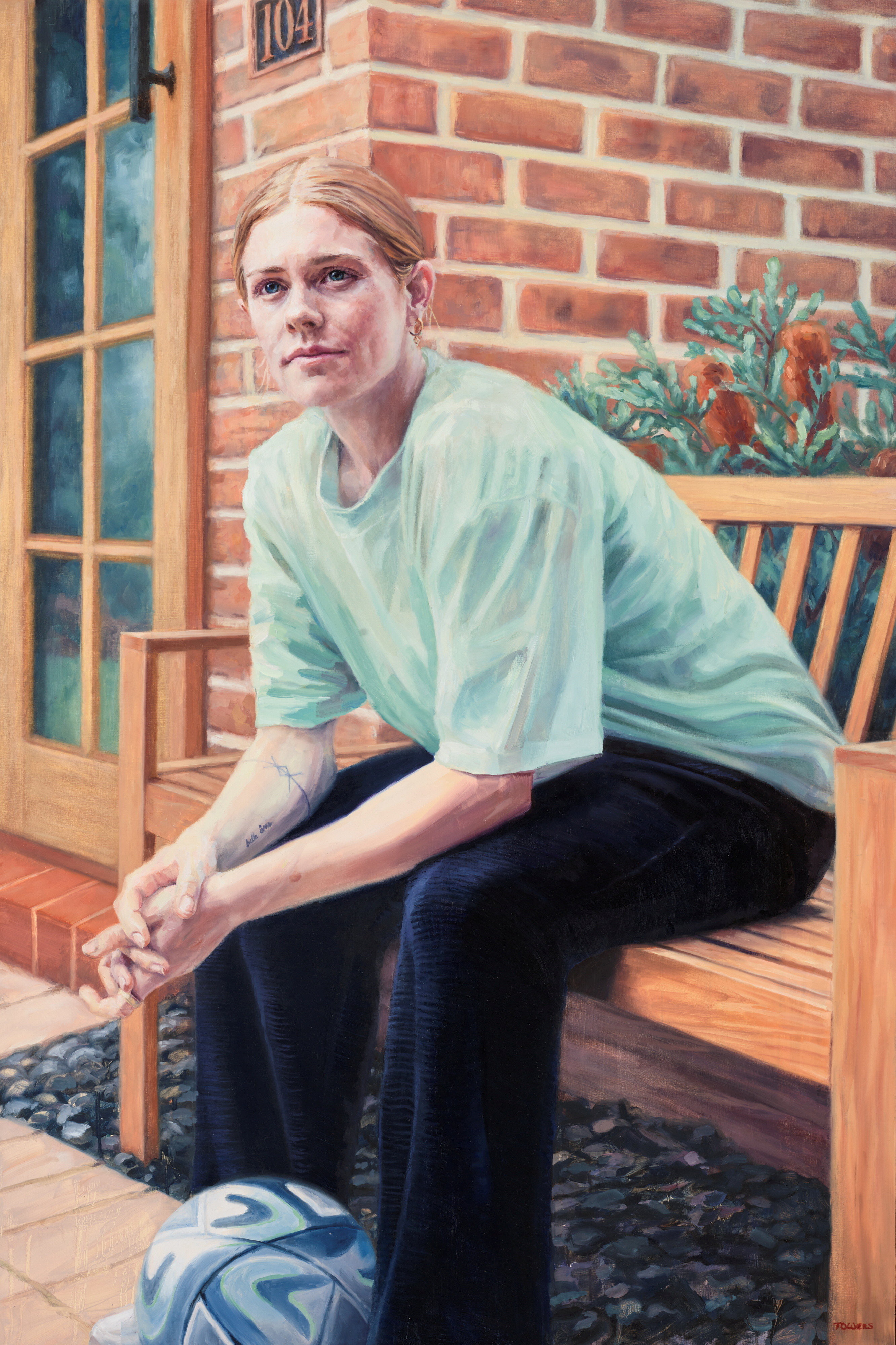 A portrait of Cortnee Vine, a white woman with red hair, sitting on a bench with a soccerball between her feet.