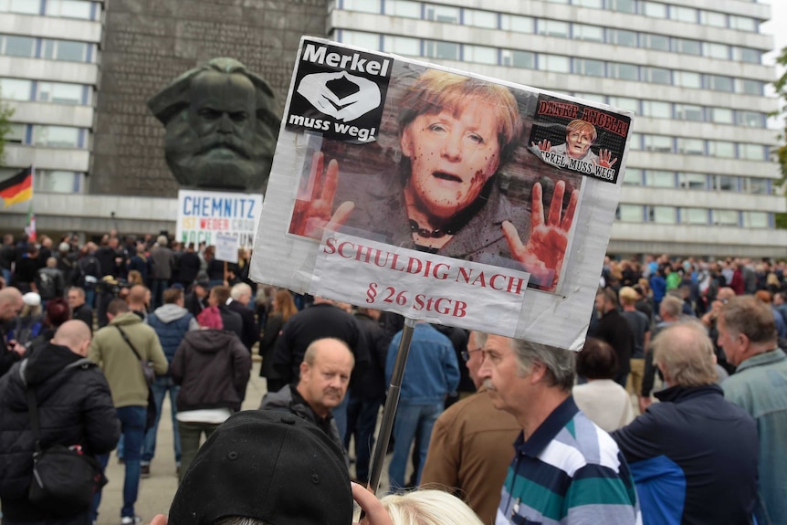 A protester holds a poster with a photo of Angela Merkel reading "Merkel must go".