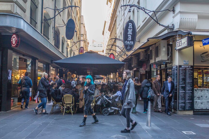 Diners crowd around tables under umbrellas in a Melbourne laneway.