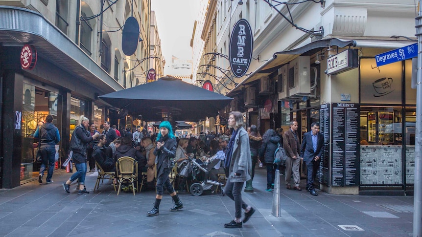 Diners crowd around tables under umbrellas in a Melbourne laneway.