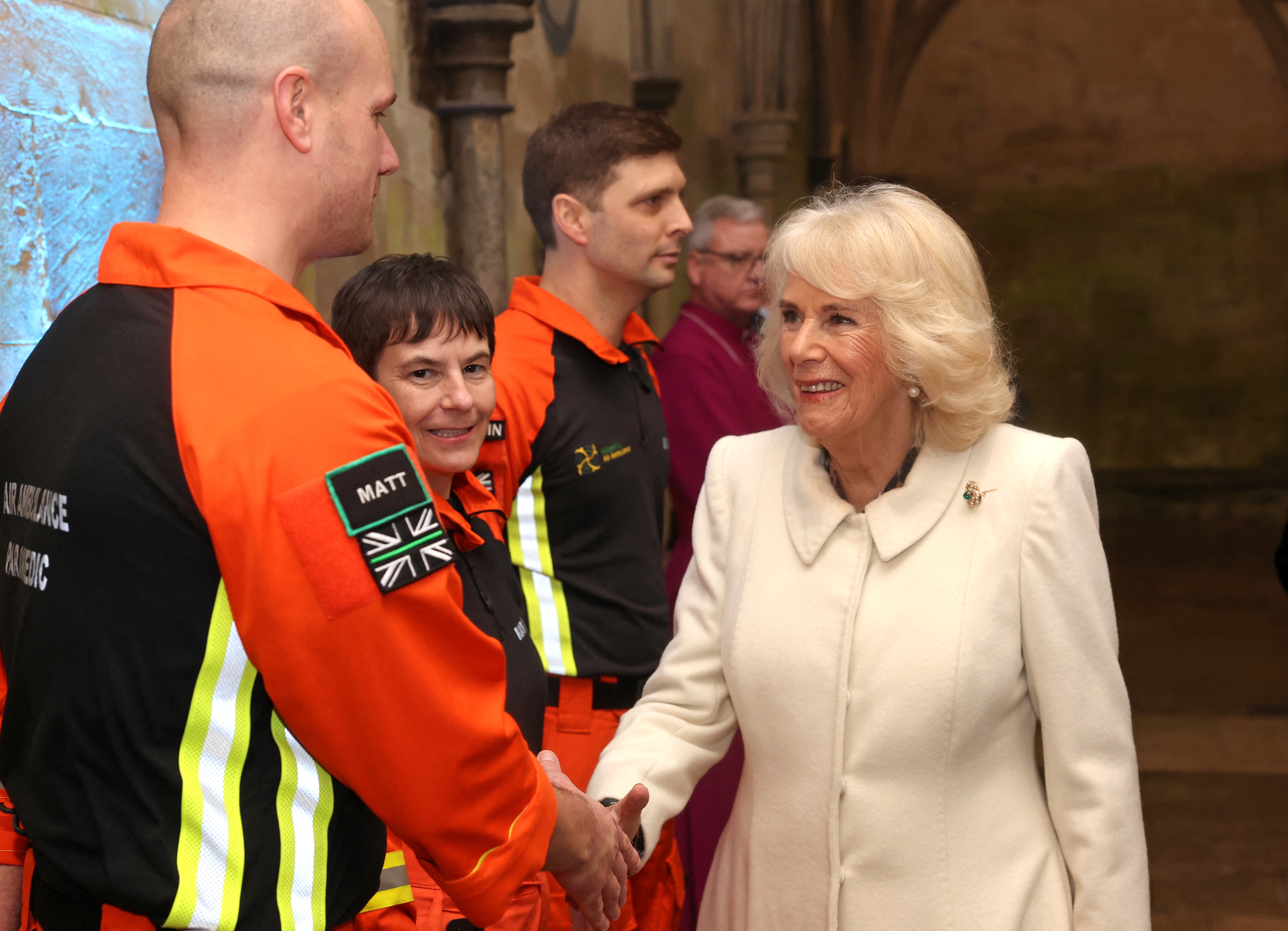A woman in a white coat shakes hands with a group of young paramedics in high vis 