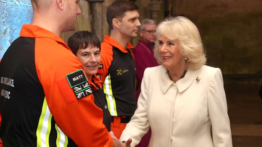 A woman in a white coat shakes hands with a group of young paramedics in high vis 