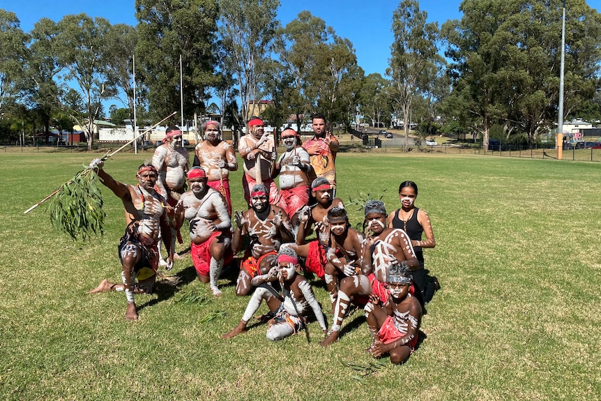 A group of Indigenous dancers in traditional garb bunched together on an oval.