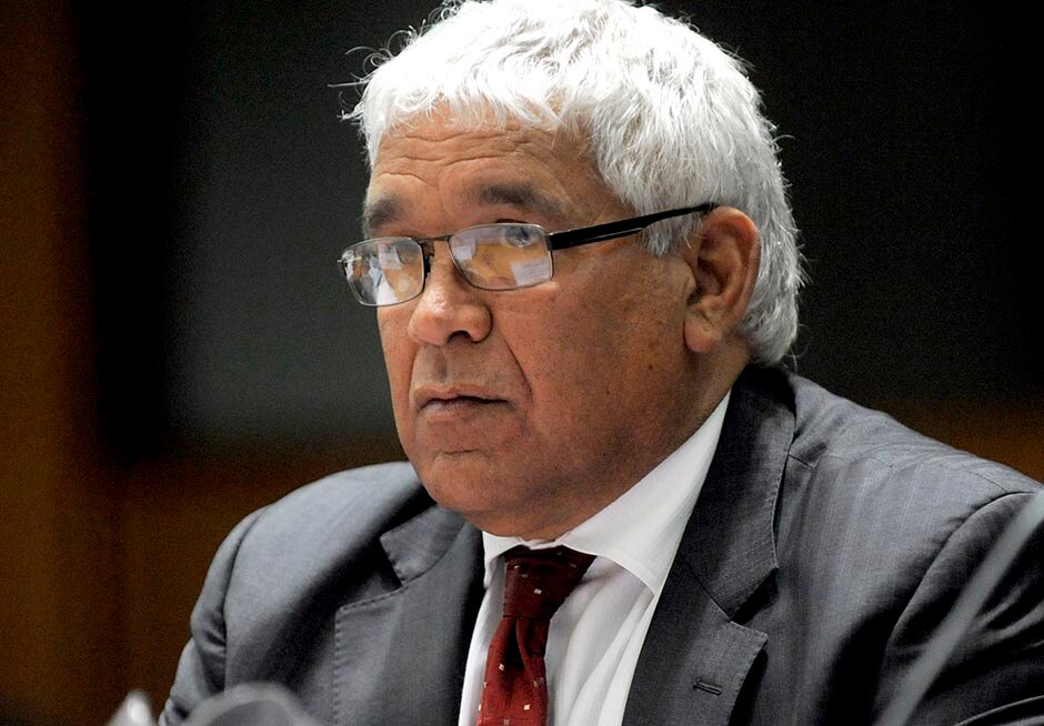 Head and shoulders shot of a grey-haired Indigenous man wearing wireframe glasses as he looks out of frame to his right.