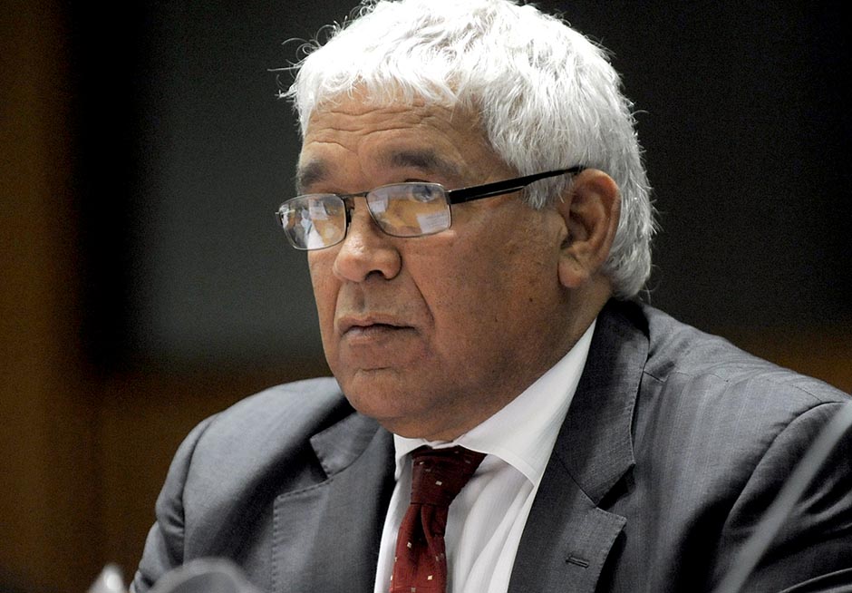 Head and shoulders shot of a grey-haired Indigenous man wearing wireframe glasses as he looks out of frame to his right.