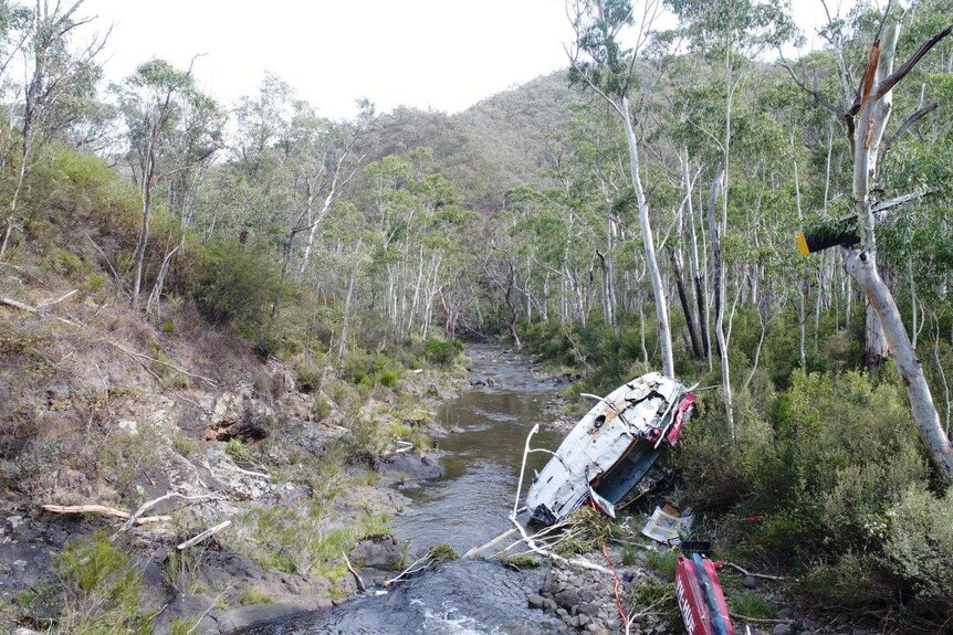 A damaged helicopter lies in a riverbed in a national park.