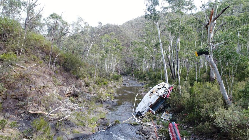 A damaged helicopter lies in a riverbed in a national park.
