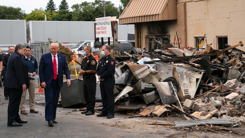 Donald Trump walks past a pile of debris as security guards wearing masks stands by.