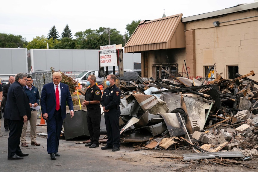 Donald Trump walks past a pile of debris as security guards wearing masks stands by.