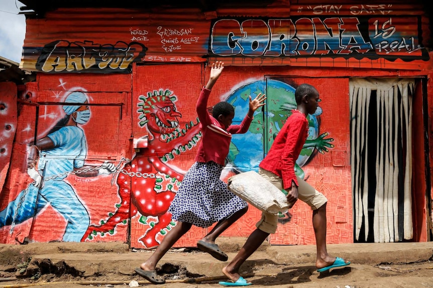 Children run down a street past an informational mural warning people about the dangers of the new coronavirus