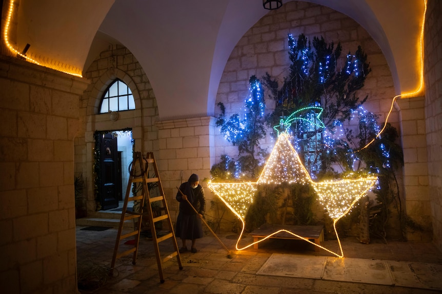 a nun wearing a mask and holding a broom sweeps the ground next to an illuminated star in Jerusalem