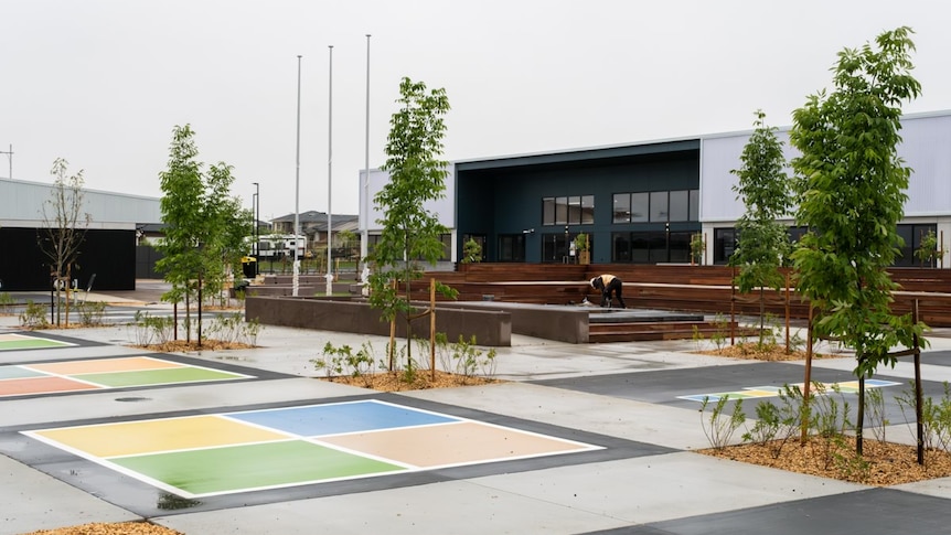 A playground with six young trees planted and a handball court.