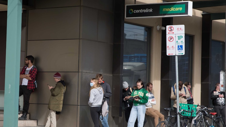 People leans against the outside of a building waiting to get into Centrelink.