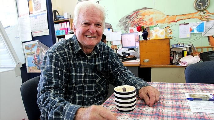 Man in check shirt sits at table drinking coffee