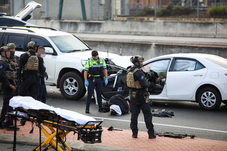 A handcuffed man lying on a road surrounded by heavily armed police.