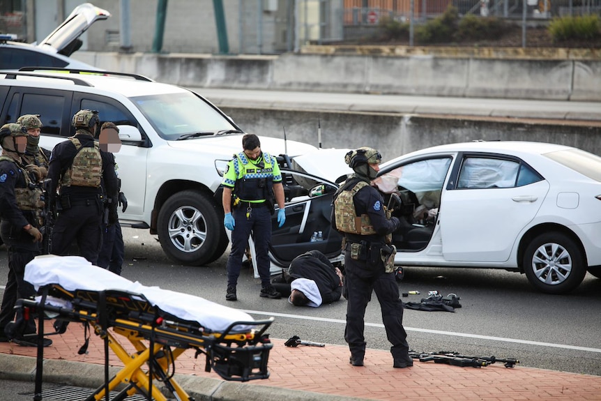 A handcuffed man lying on a road surrounded by police.