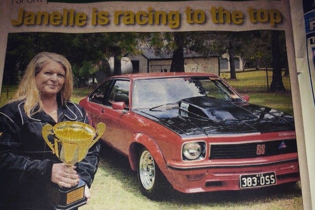 A newspaper clipping showing a woman in front of a car holding a trophy