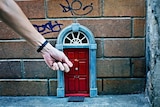 A hand reaches down to knock on a little red door on a wall in Brisbane CBD
