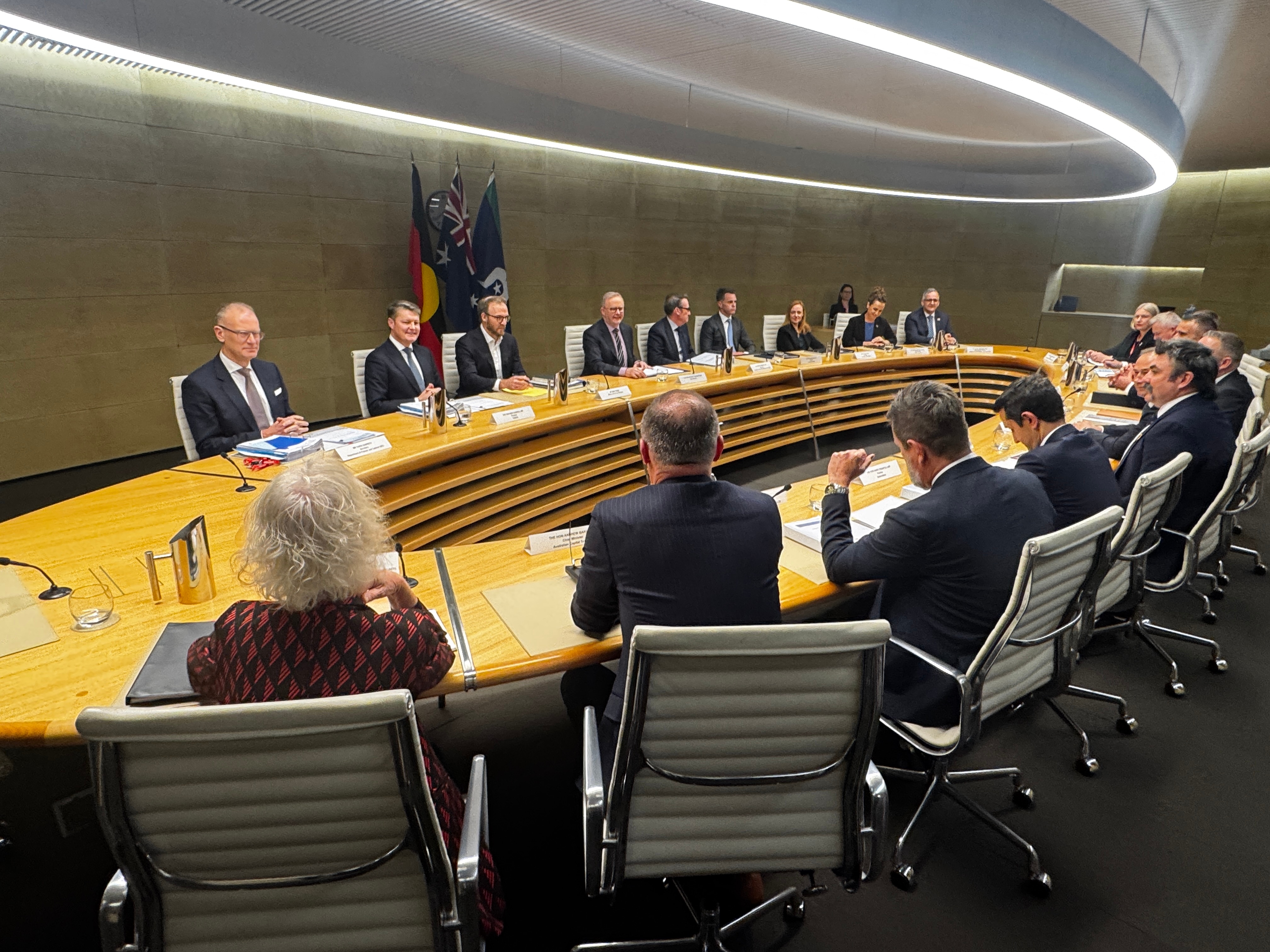 An oval table with people sitting on either side, viewed from behind one side.