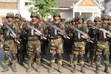 Cambodian men in army fatigues stand to attention holding rifles.
