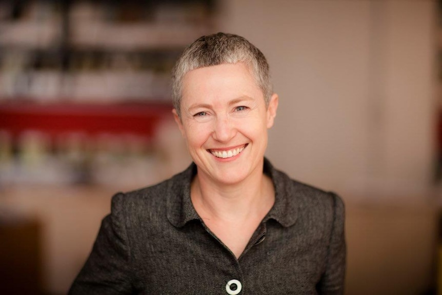A woman in a black shirt with short gray hair smiles at the camera
