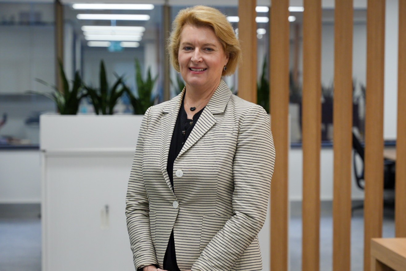Woman swearing a suit standing in the middle of an open plan office, smiling.