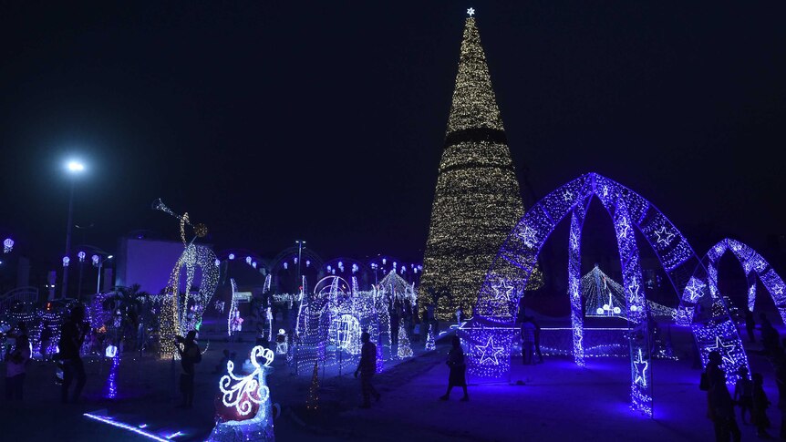 People walk around a large Christmas tree, coloured purple, in Owerri, Nigeria, at night on New Year's Eve.