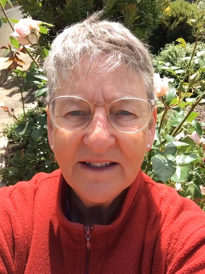 A woman with short grey hair and clear rim classes wearing an orange zip fleece