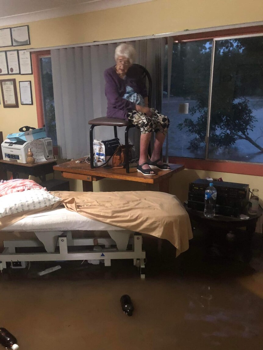 elderly woman sitting on a chair, on top of a table, on top of a bed as flood waters fill a room