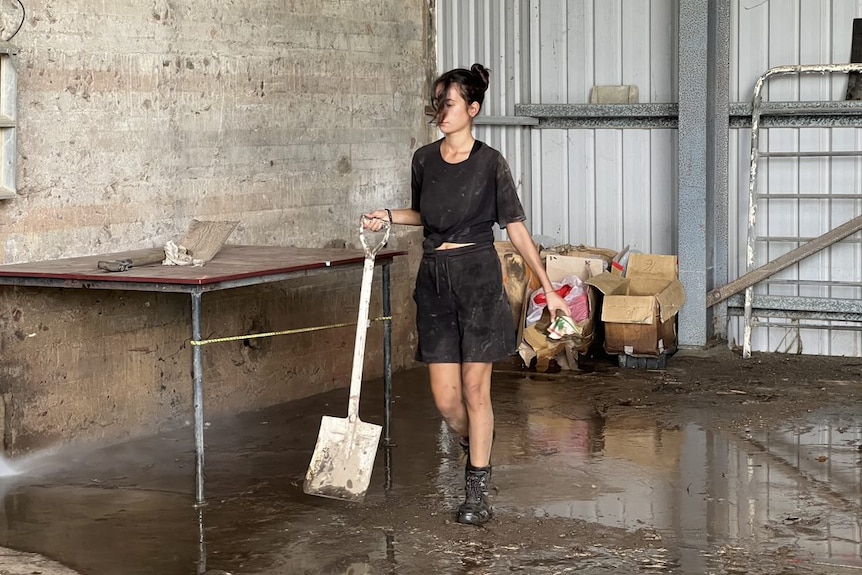 Woman dressed in black holds a shovel in a muddy shed.