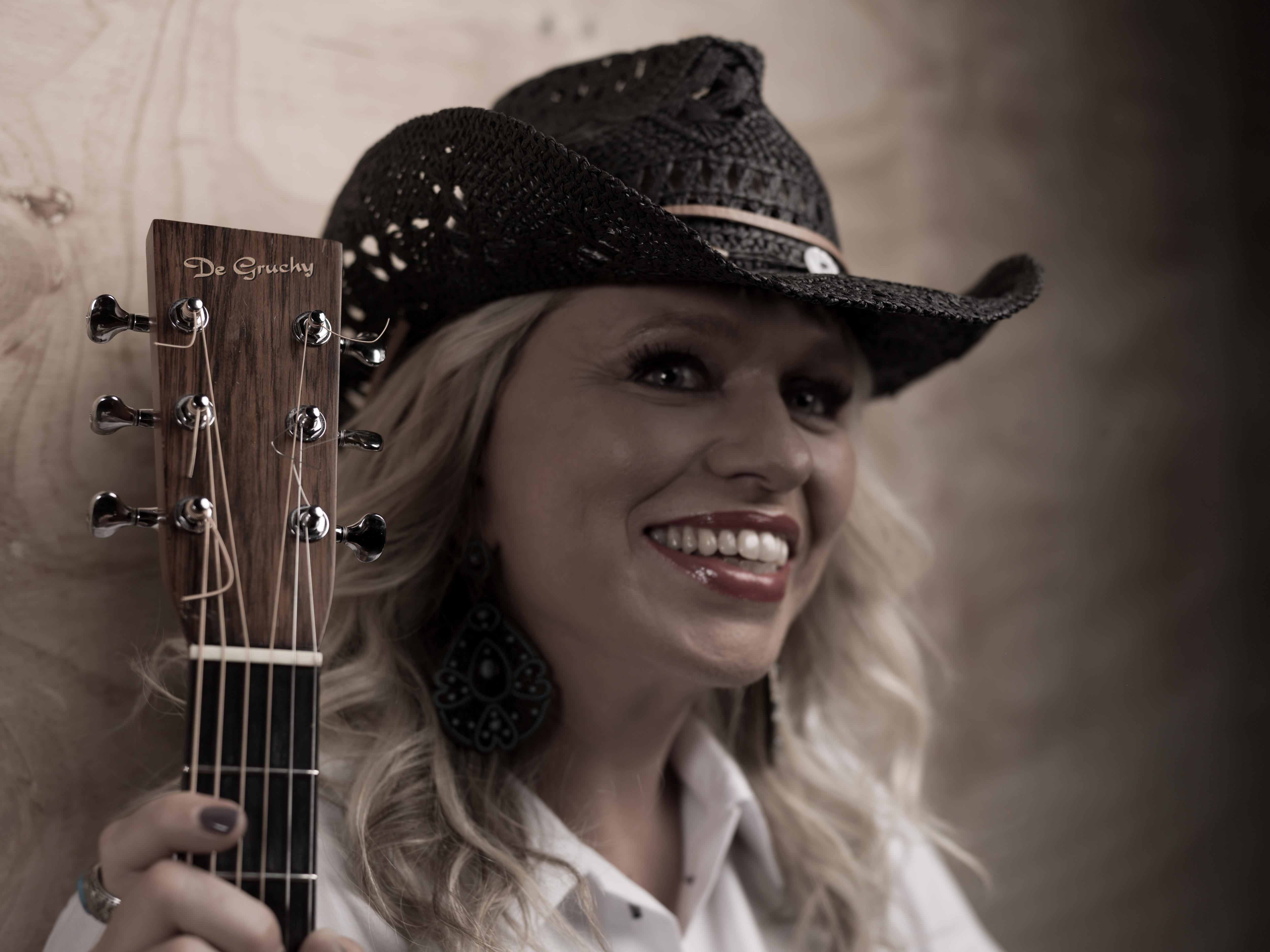 Australian Country legend Beccy Cole smiles with a cowboy hat and holds a guitar neck