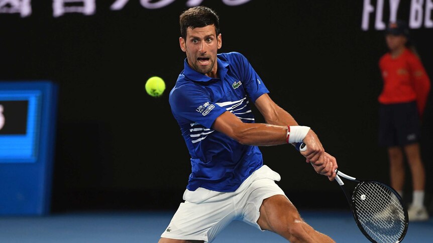 Novak Djokovic makes a leap for the ball, legs stretched wide.