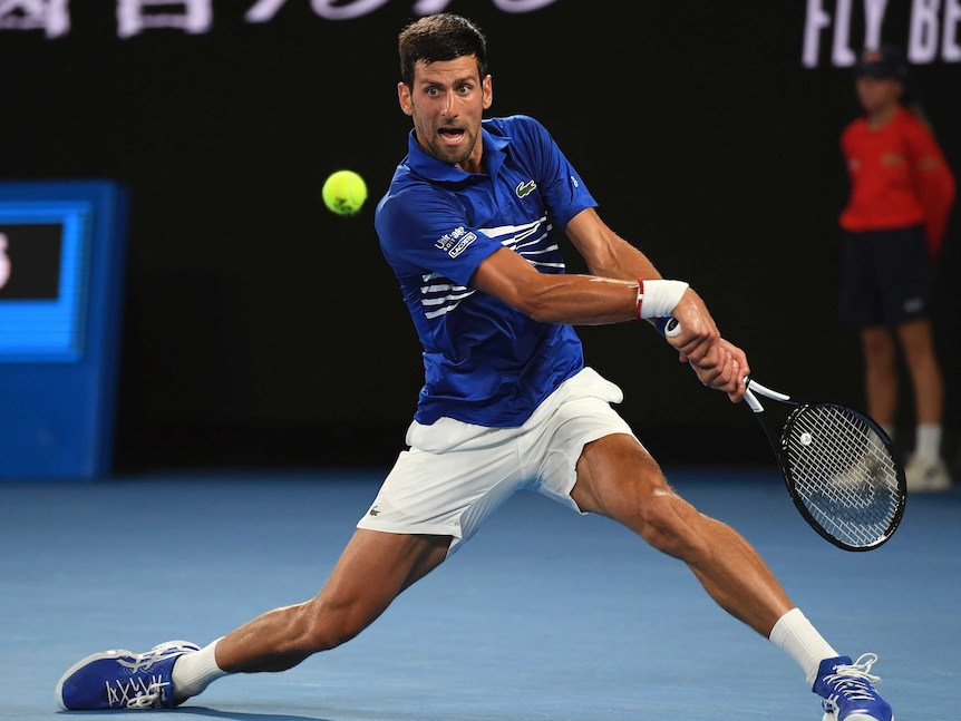 Novak Djokovic makes a leap for the ball, legs stretched wide.
