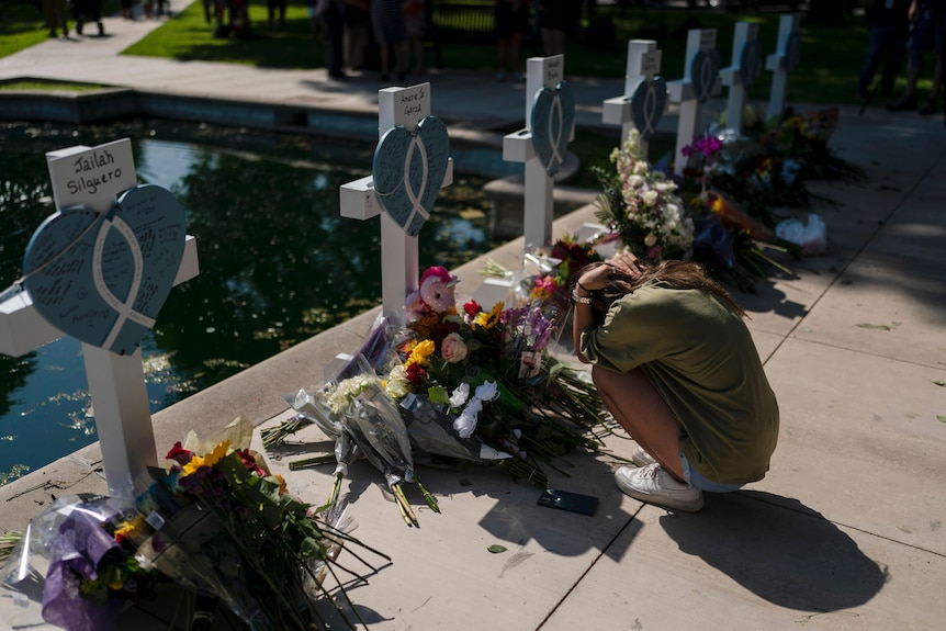 A woman grieves in front of a cross honoring her cousin