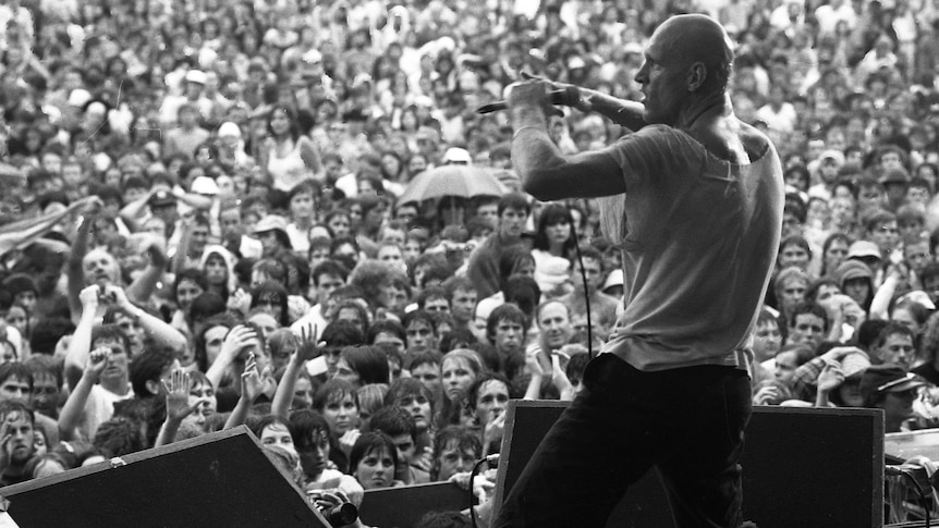 Bald headed man in front of a large crowd