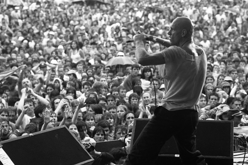 Bald headed man in front of a large crowd