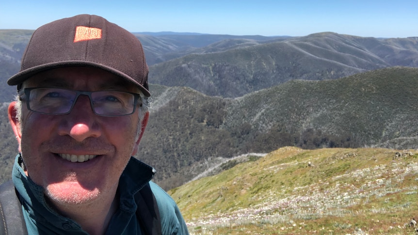 A selfie of a man smiling at the camera, with Victoria's mountains behind it