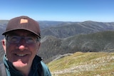 A selfie of a man smiling at the camera, with Victoria's mountains behind it