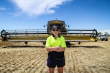 Mary-Anne Pollard standing in a field of barley in front of a giant header machine used for cropping.