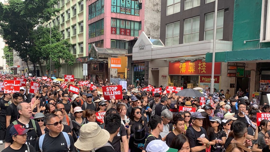 Hong Kong protesters dressed in black carry signs that read "Stop killing us".