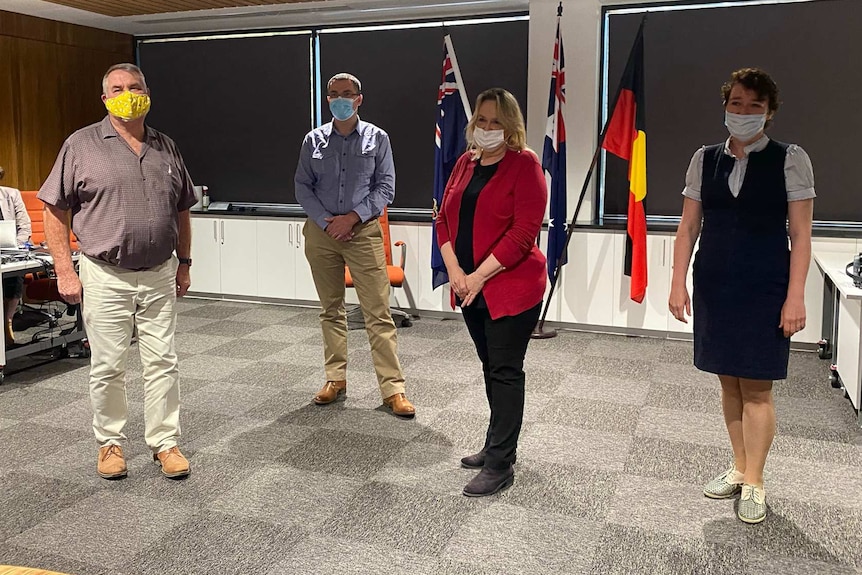 four people stand next to each other socially distanced wearing masks