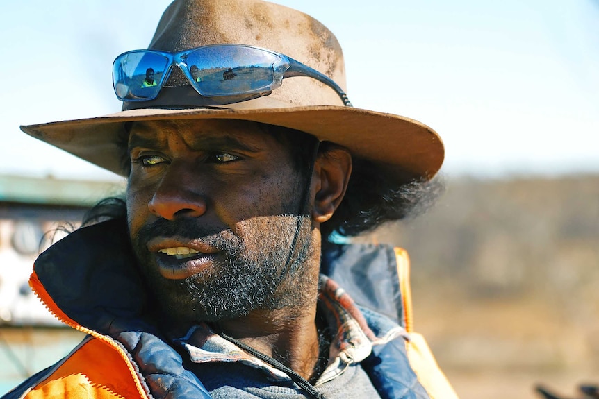 A man with a wide brimmed hat looks out to the distance.