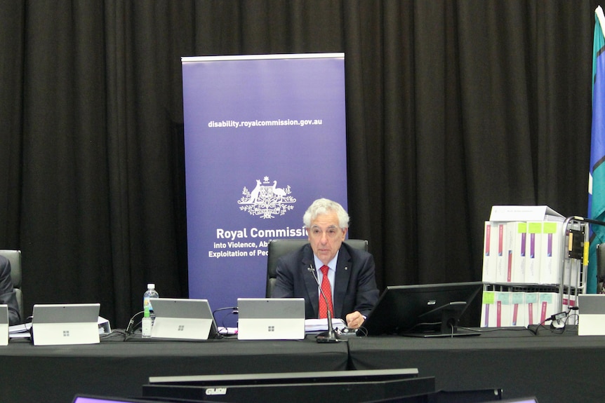 The disability royal commissioner sitting at a desk at a public hearing