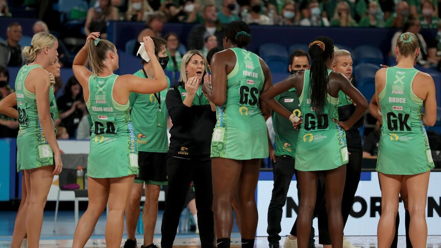 West Coast Fever coach Stacey Marinkovich chats to players in a huddle with green dresses on.
